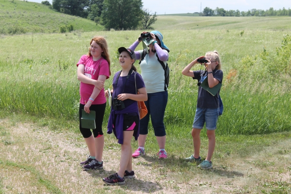 An educator and 3 campers on the trail observing flying birds in summer