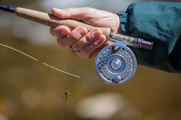 hand of man holding reel of a fly fishing pole