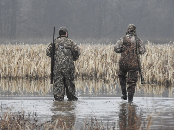 An image of two hunters in camo walking through water.