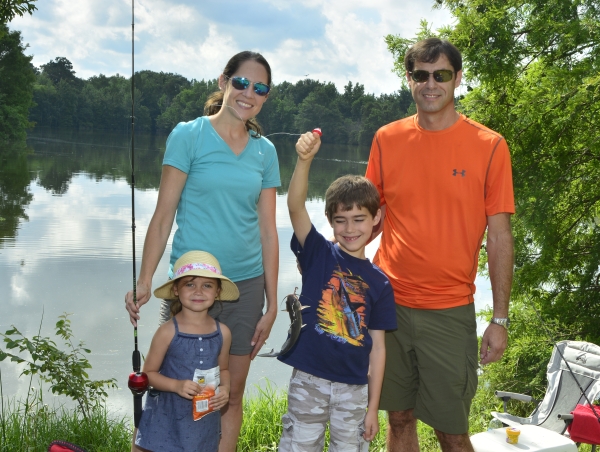 Woman, man, girl, boy standing in front of pond with fishing pole and fish