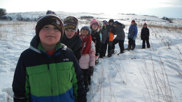 Several children in a line on snowshoes in the snowy prairie