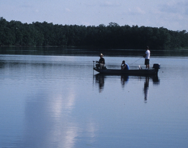 Three men fishing from small boat on river