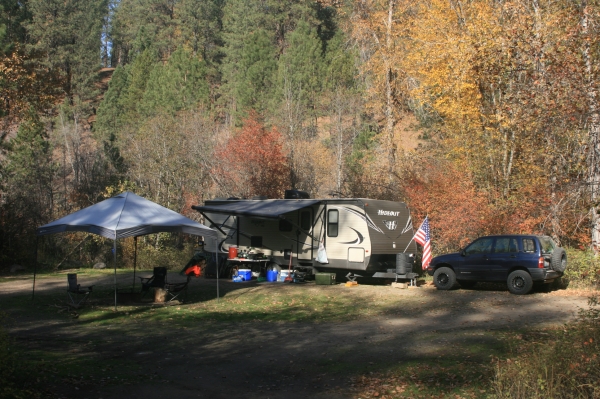 Camping setup with an RV, car and canopy. Located in a mixed conifer forest.