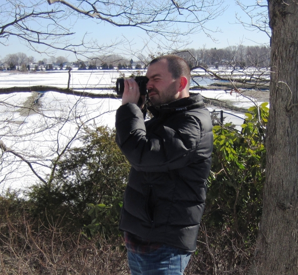 A photographer focuses his camera on a bird that he sees near the salt marsh.