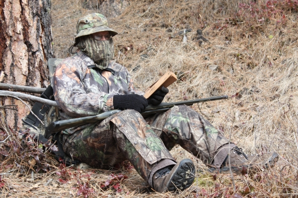 Hunter sitting at the base of a tree, wearing camouflage and turkey calling.