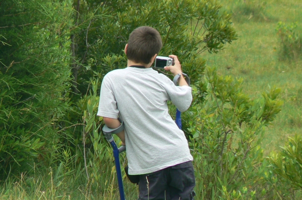 A child leans on forearm crutch while taking a photo