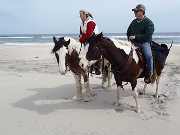 Two people sit on horseback on the beach