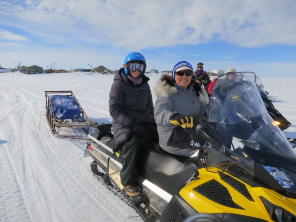 several people in winter gear and helmets sit on snowmobiles along a snowy trail