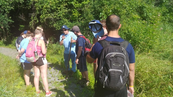 Volunteer leading a group on a nature walk with lush green shrubs in the background.