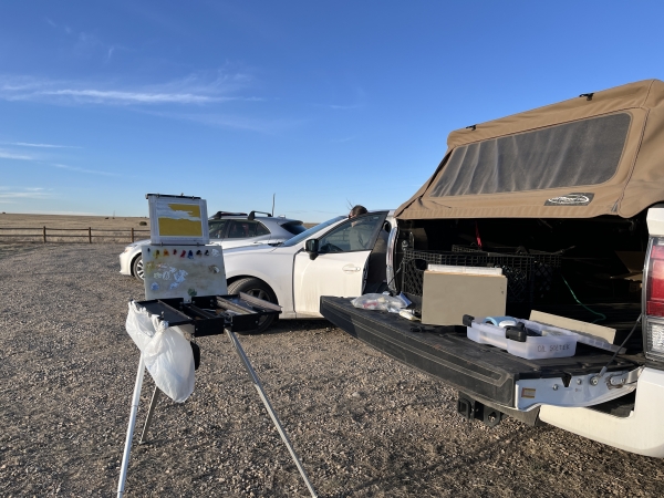 A painters set up on an easel and in the back of a covered pickup truck.