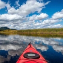A bright blue sky obstructed by fluffy white clouds reflected off of a stream shot from inside a kayak
