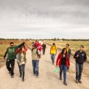 A group of 13 youth and staff members walk down a dirt and gravel road with a field on their side