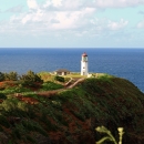 A lighthouse stands on the edge of a peninsular cliff with a large ship in the s