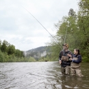 A parent and child stand in a river, fly fishing.