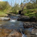 A stream flows under a small bridge in wooded area.