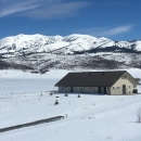 House perched in a snowy meadow, below snow capped mountains. 