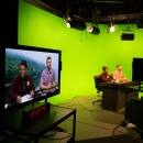 man and woman sitting at news desk with green screen in background of broadcasting studio