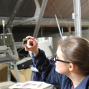 A young woman in glasses holds a slide up to look at it in an attic storage space.