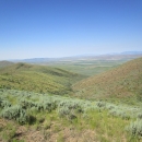 A view of rolling hills can be seen with green vegetation and sagebrush.