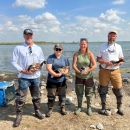 4 biologists are each holding a duck standing in front of a wetland 