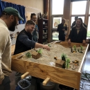 People standing around a table filled with gravel, miniature trees, and miniature sheds
