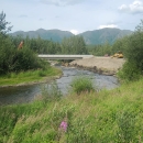 a bridge over a river in the distance with mountains in the background and pink fireweed flowers in the foreground
