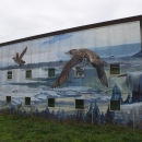Small, chubby marbled murrelets fly over a coastal landscape consisting of redwoods and ocean coves in this mural painted by Lucas Thornton in Arcata, CA
