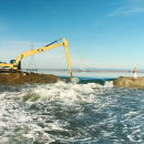 A bulldozer works to remove part of an earthen levy separating two bodies of water.