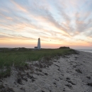Sandy barrier island beach at sunset with lighthouse in the distance.