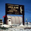 A Jarvis Island sign is posted in front of a camp site. It is wood with yellow words.