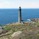 A scenic view of grassy hills and a white lighthouse on the coast of Thacher Island, with the ocean in the background