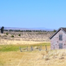 An old stone A-framed building in a high desert landscape with an old mill next to it