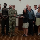 A man in fatigues accepts an award from a woman in a U.S. Fish and Wildlife Service shirt with a group of other people standing around them