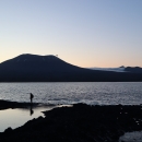 Biologist walks along shore of St Lazaria island at dusk with Mount Edgecumbe in the background.