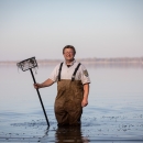 Man stands in water wearing waders as he is holding a net.