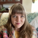 a woman with light brown hair and bangs sits on a couch