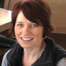 A portrait of a woman smiling from her shoulders up with short auburn hair