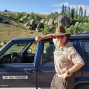 A man leaning against a blue jeep wearing a fish and wildlife service uniform