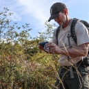 Male biologist stands in a field with a phone and glass jar in his hands