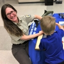 Woman in FWS uniform smiles while teaching a child about salmon at an education event