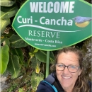 Cartherine smiles in front of a green sign that says 'Welcome Curi-Cancha Reserve'