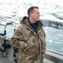 Man dressed in camouflage on a boat surrounded by a glacier