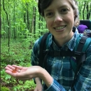 Clare smiles holding a small red salamander in a blue flannel