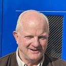 man in brown vest stands in front of a blue door
