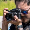 A guy with sunglasses looks through a camera lens
