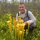 Man in a forest crouched over and smiles, next to bright-yellow pitcher plants.