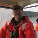Man sitting on boat in orange float coat with binoculars around neck