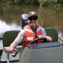 Service employee wearing an orange lifejacket driving a jon boat with an outboard motor. 