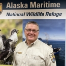 Man stands in front of mural with birds and the words Alaska Maritime National Wildlife Refuge