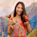 A woman wearing a red dress holds several native Hawaiian forest birds